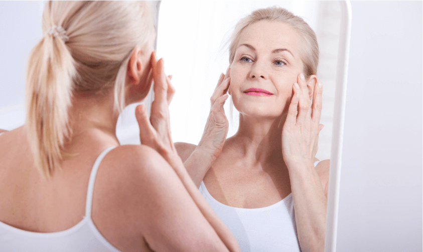 Mature woman examining her skin in the mirror and touching her face