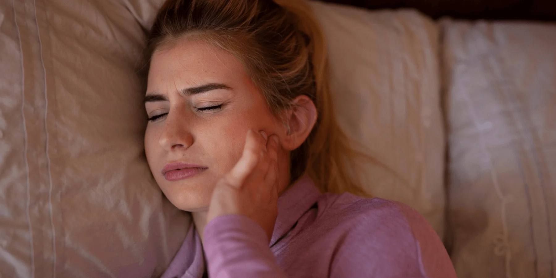 Woman holding her jaw in pain while lying down, showing TMJ discomfort.